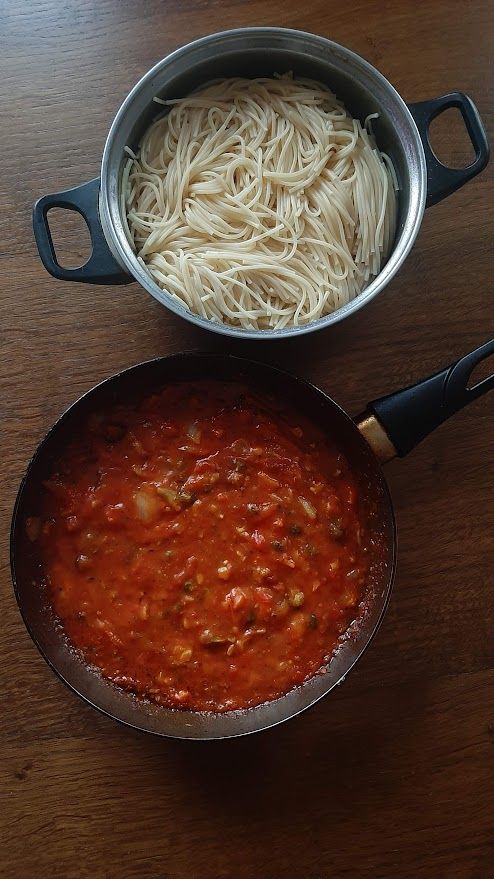 a pan with tomato sauce and a pot full with spaghetti